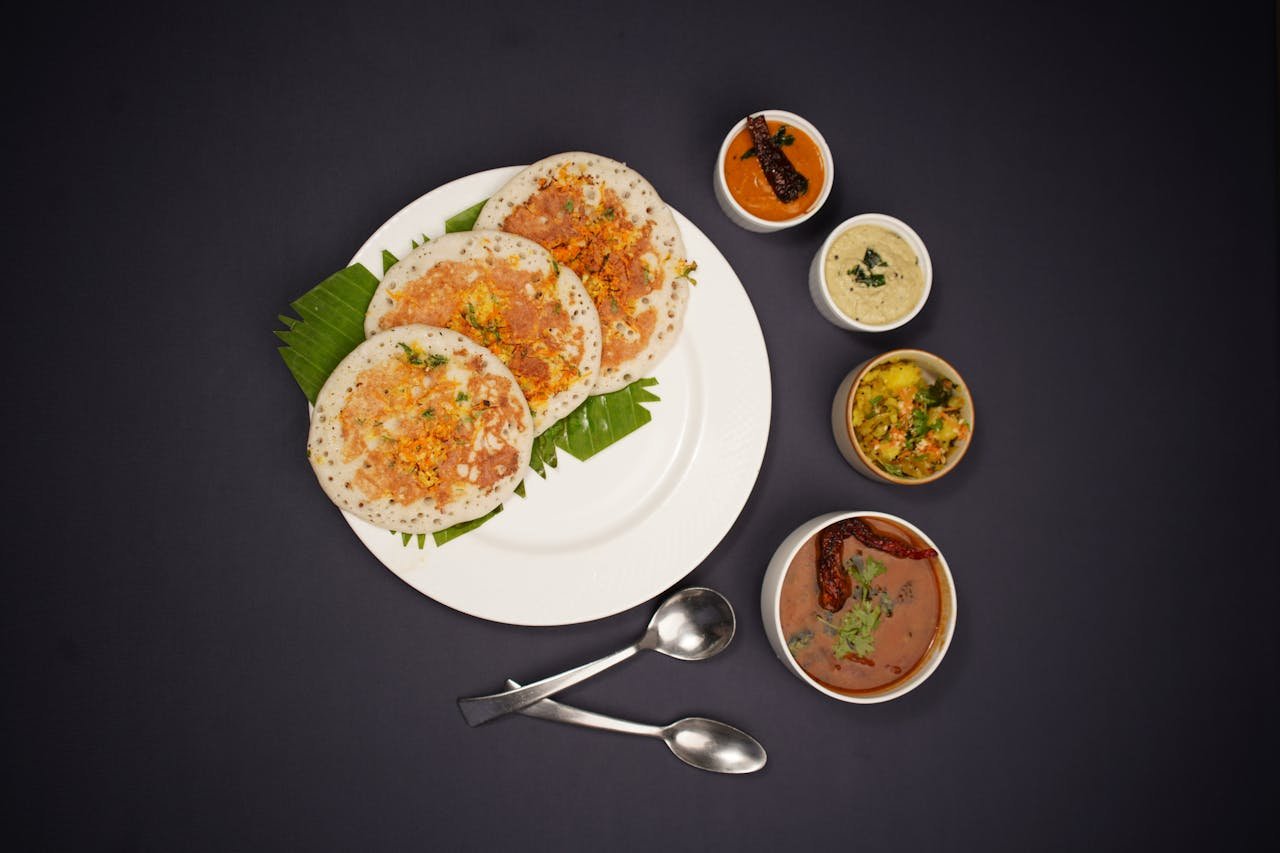 Top view of South Indian dosa served with a variety of chutneys on a black background.